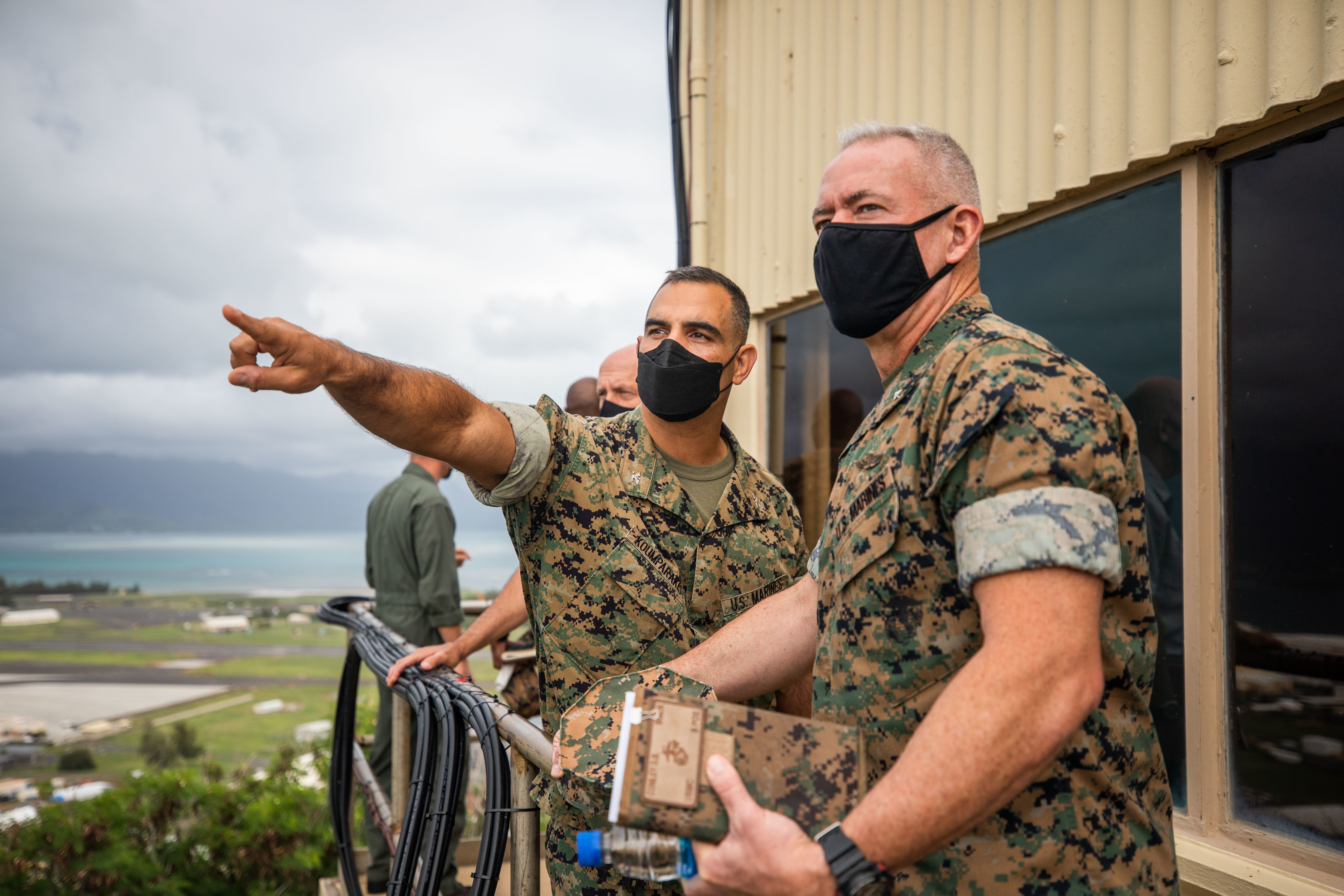 A few Marines in uniform standing on a balcony, one pointing out at something.