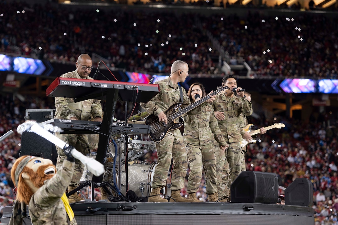 A group of airmen play music and sing on stage in a stadium.