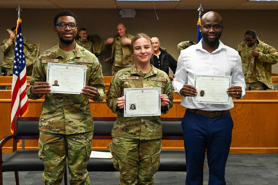 Airman 1st Class Jarious George from the 5th Force Support Squadron, Airman 1st Class Kojo Affainie and Airman Constanza De Puerta, from the 5th Logistics Readiness Squadron, earn their United States citizenship during a naturalization ceremony, Nov. 15, 2022, at Minot Air Force Base, North Dakota. During the ceremony, the Airmen were presented with their Certificates of Naturalization, making them U.S. citizens by law. (U.S. Air Force photo by Senior Airman Zachary Wright)