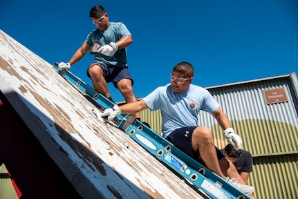 Two men work to remove old old paint from wood