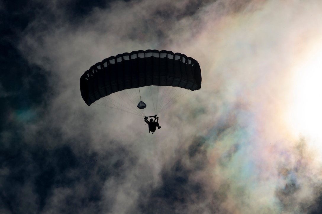 An airman free falls with a parachute among clouds and a rainbow.