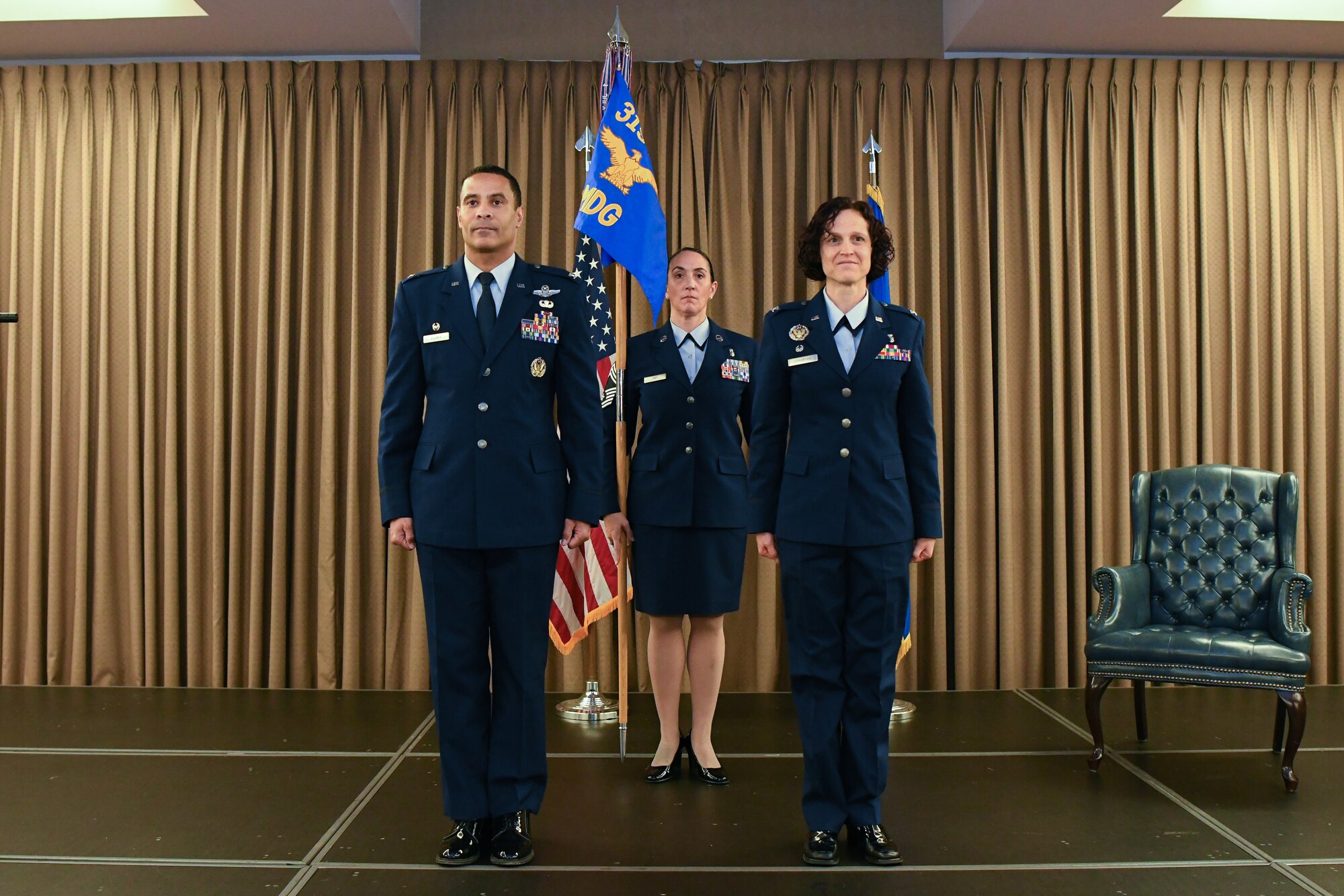 Three people in blue uniforms stand on stage during a ceremony.