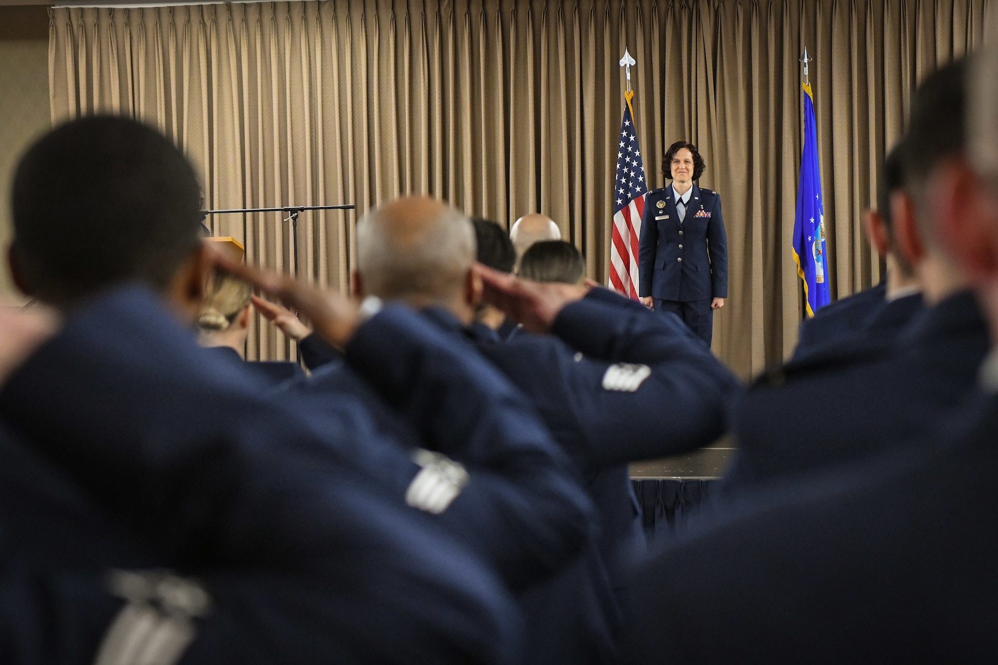 People in blue uniforms salute a woman standing on a stage during a ceremony.