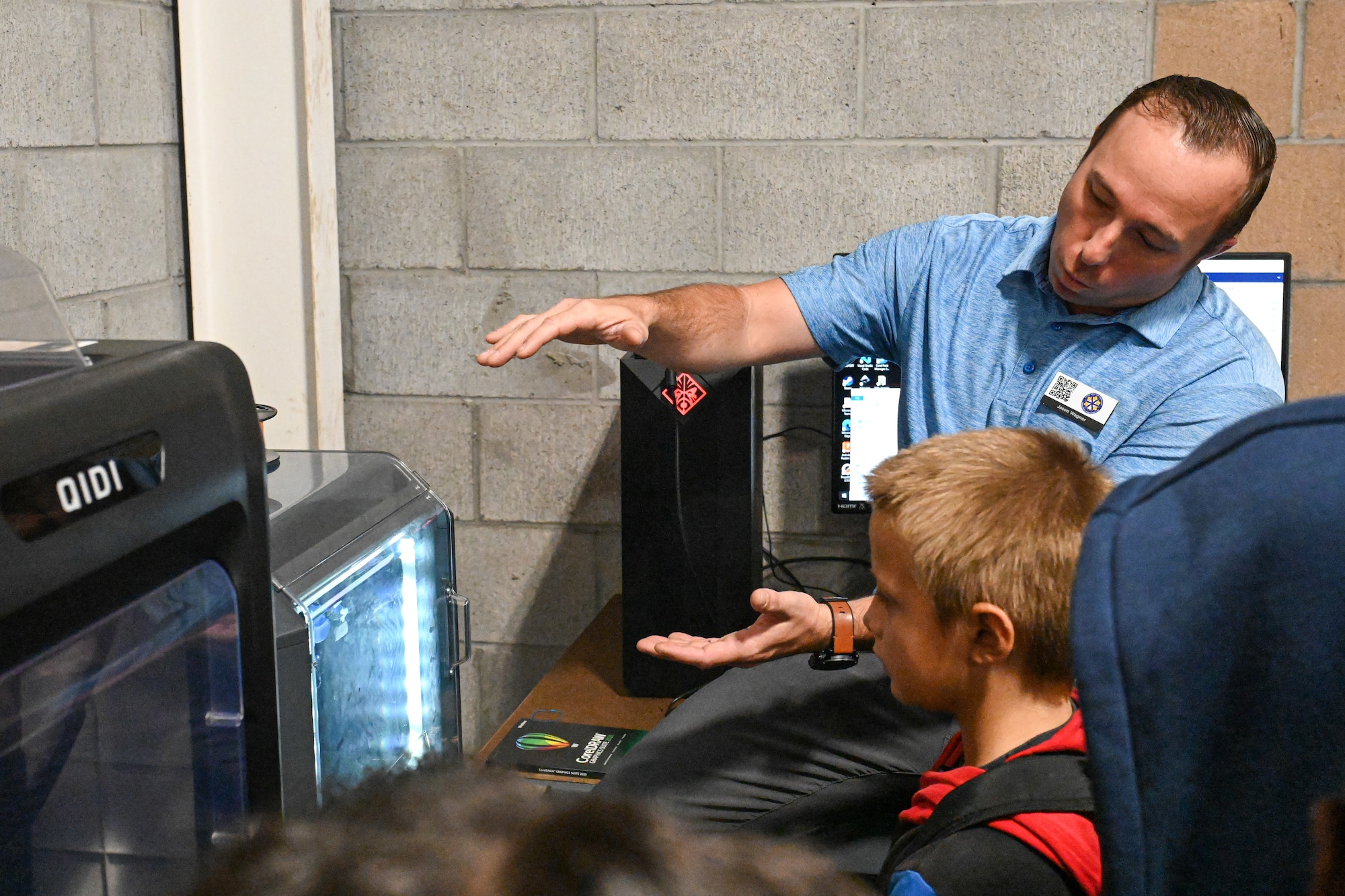A man shows a 3D printer to a child.