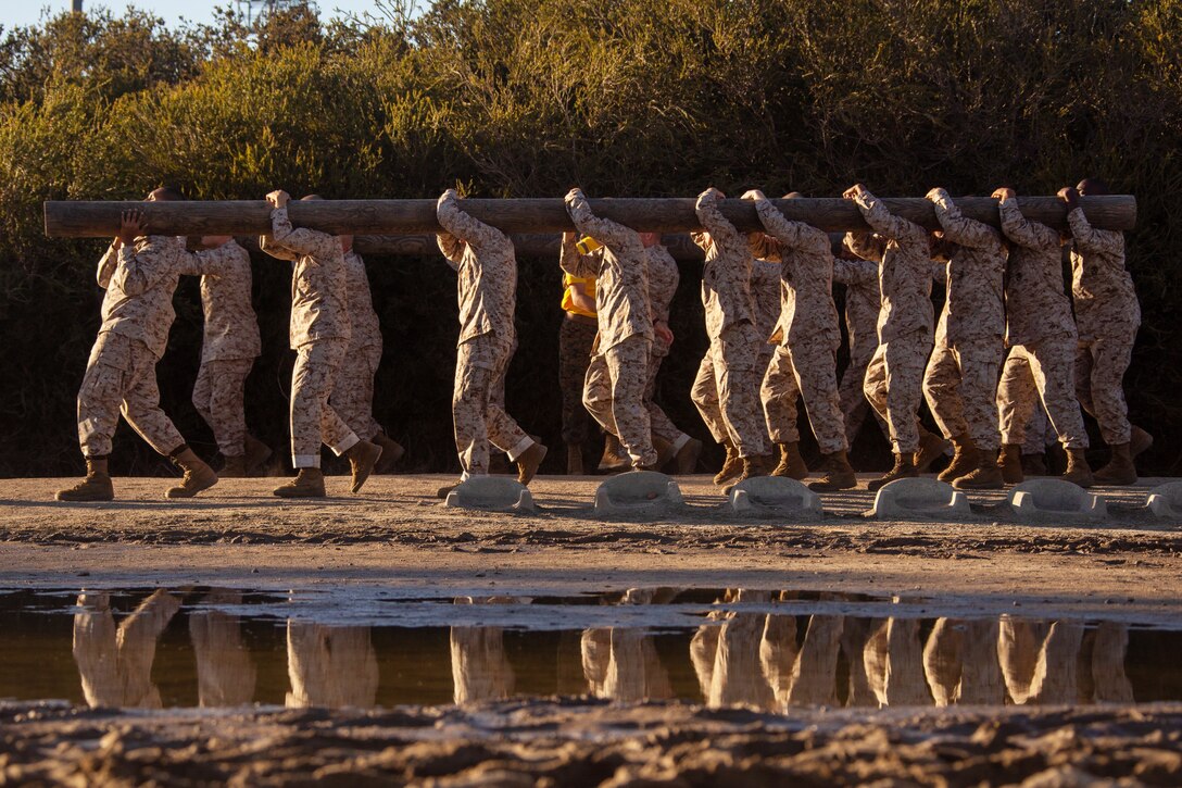 A group of Marines walk and carry a large log.