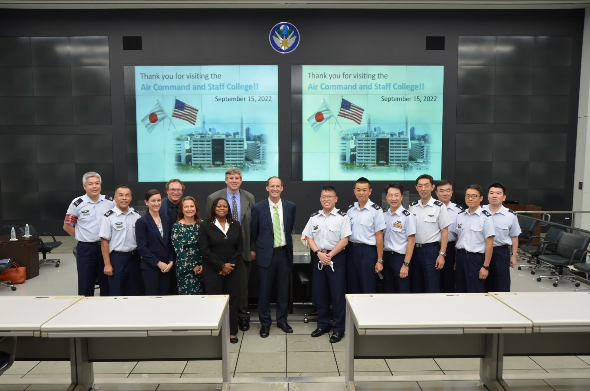 Faculty members from Air War College and the Japanese equivalent standing together for a photo in front of a screen