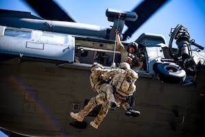 Photo of Airmen on a hoist connected to a hovering helicopter