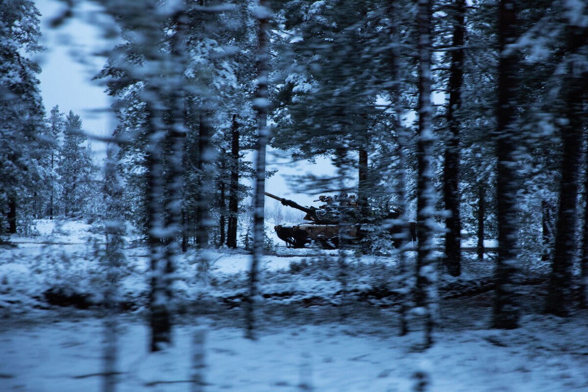 A tank speeds through the woods in the snow.