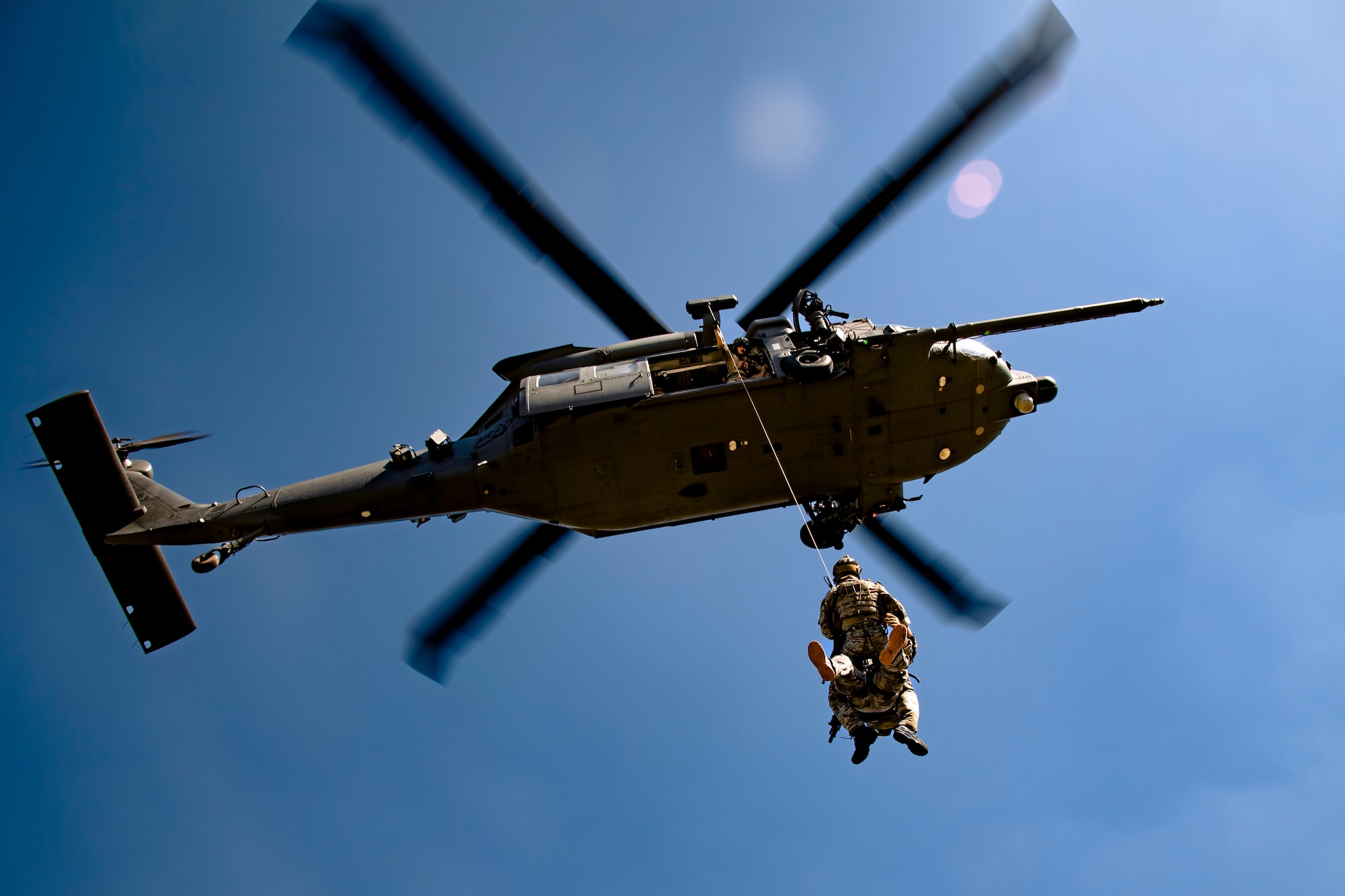 Photo of Airmen on a hoist connected to a hovering helicopter