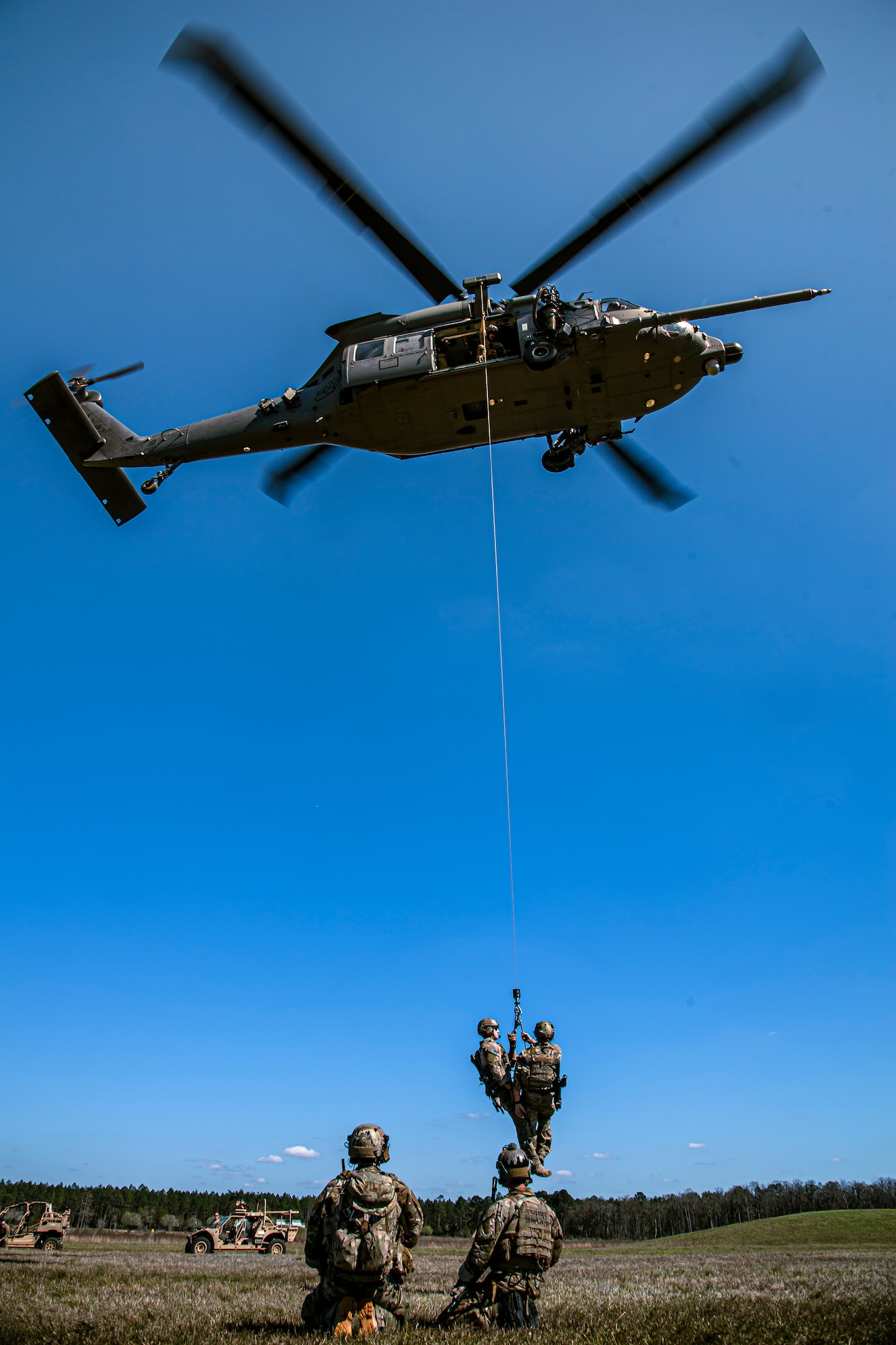 Photo of Airmen on a hoist connected to a hovering helicopter