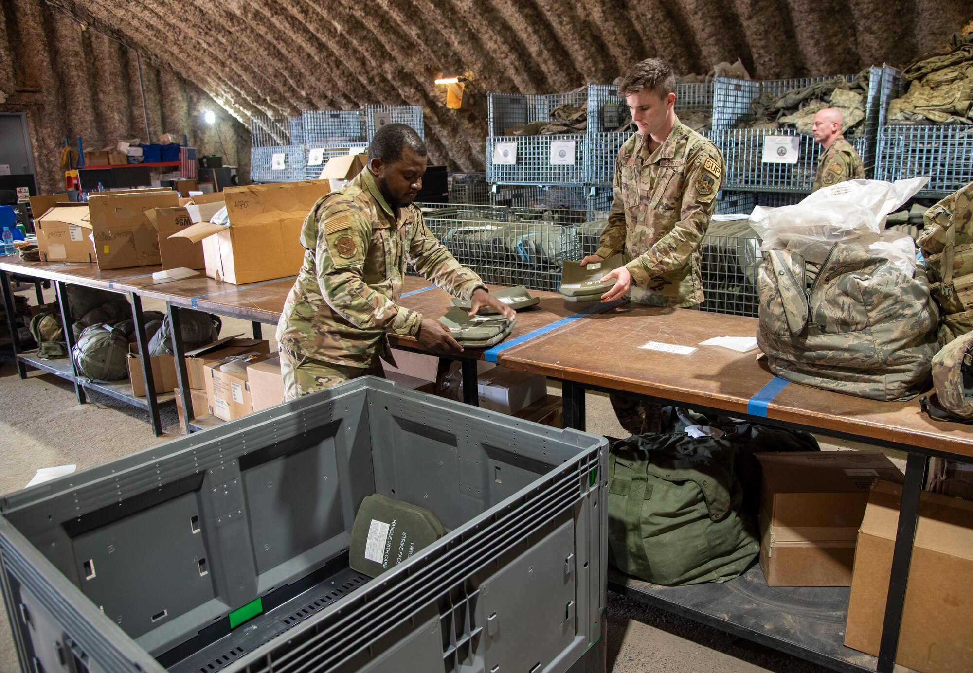Senior Airman Joseph Essilfie (left) and Airman 1st Class Jake Gaffney, 332d Expeditionary Logistics Readiness Squadron Individual Protective Equipment personnel, load ballistic plates into a crate at an undisclosed location, Southwest Asia, Nov. 11, 2022. These plates must be regularly shipped to testing facilities to ensure their structural integrity and continued effectiveness in body armor. (U.S. Air Force photo by: Tech. Sgt. Jim Bentley)