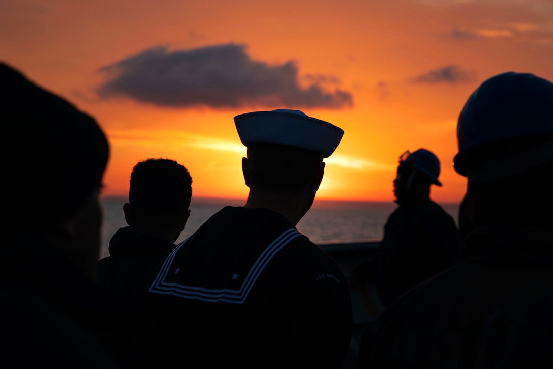 Sailors gather on a ship at twilight.