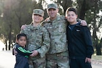 Two service members stand with two children