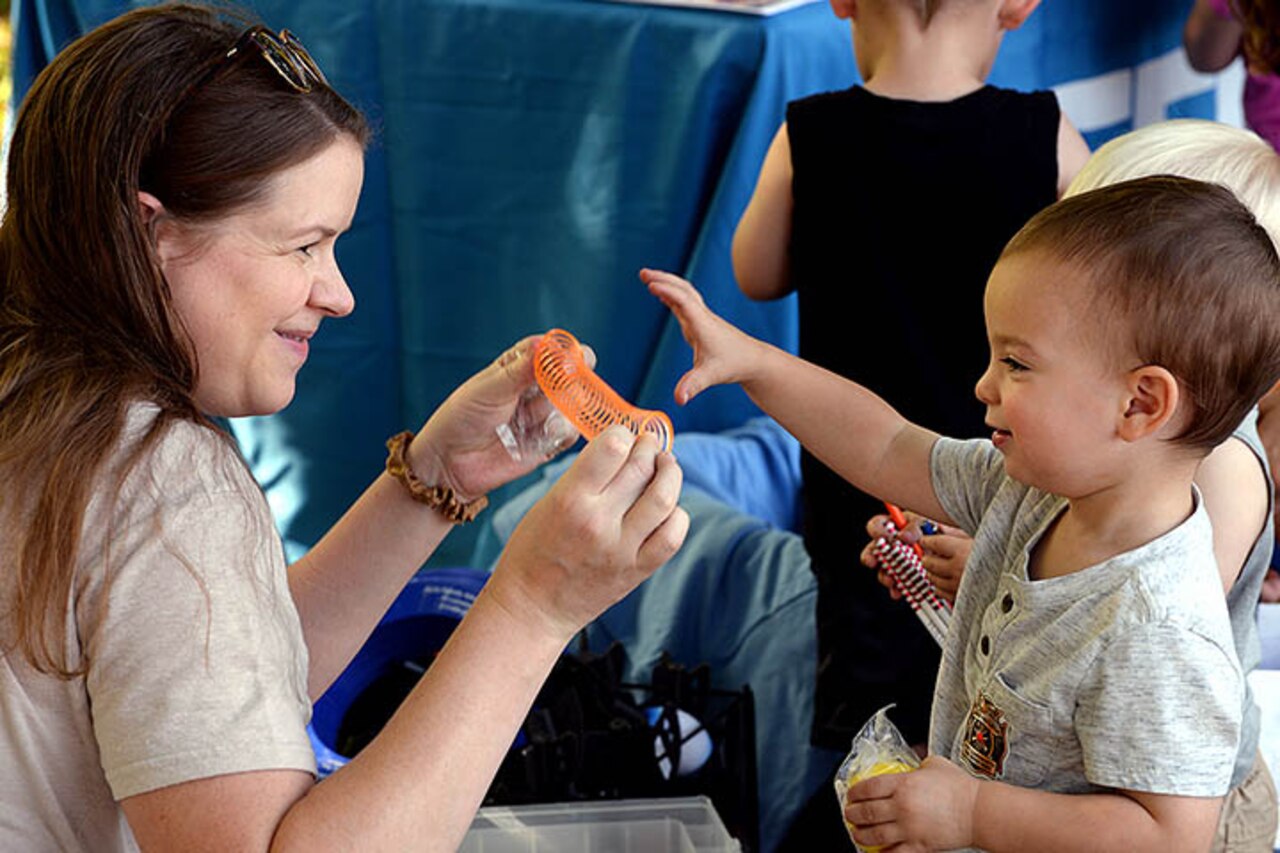 An adult woman holds an orange spring. A small child reaches for the toy.
