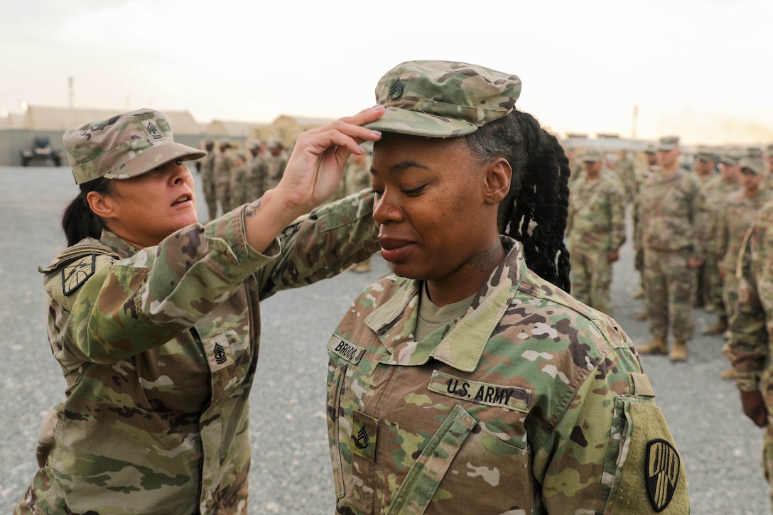 A soldier places a new cap on another soldier's head during a ceremony.