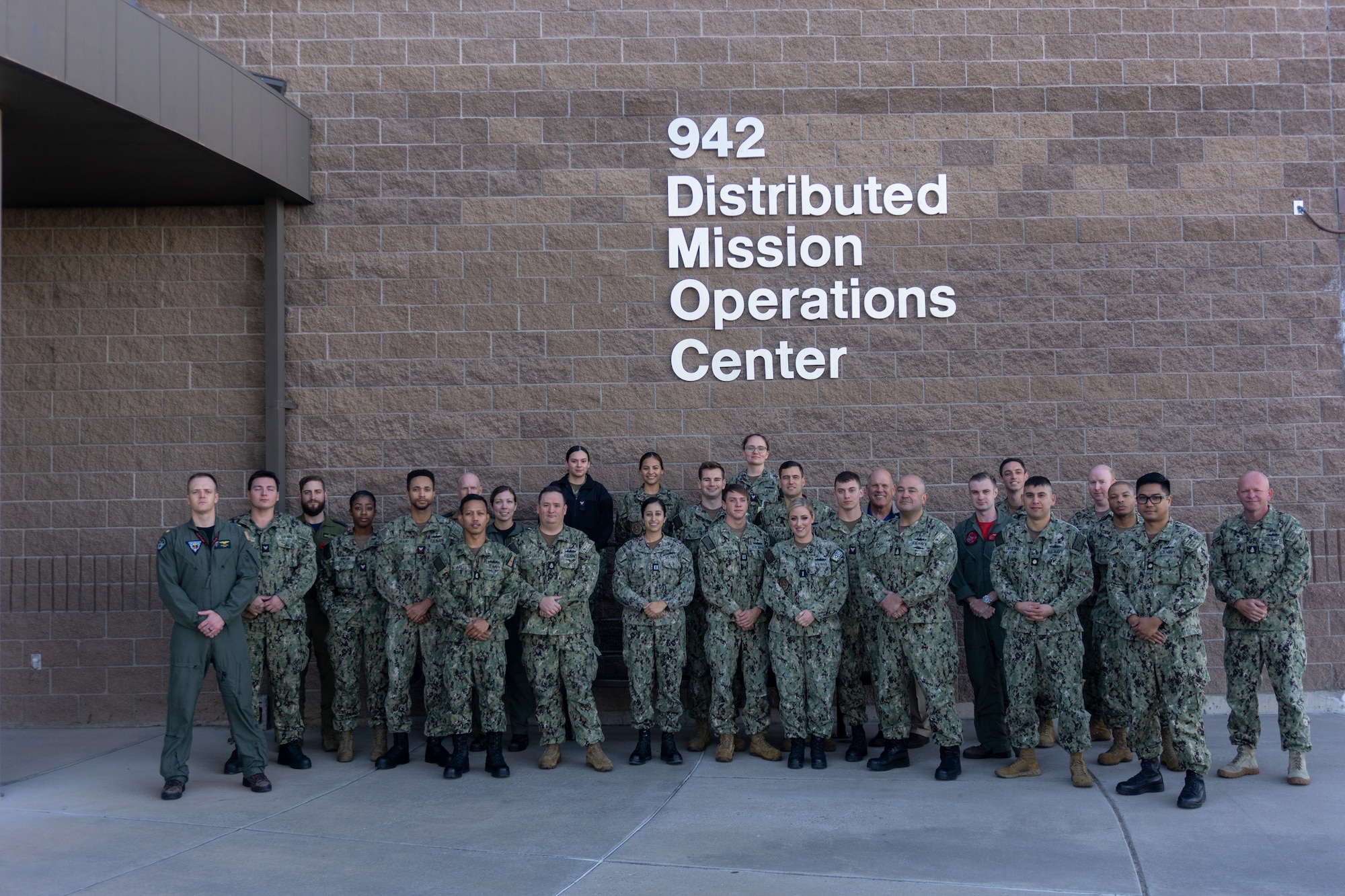 photo: military members stand in a group in front of building with wording “942 Distributed Mission Operation Center”