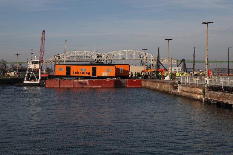 A barge carries four construction trailers through the Poe Lock and delivers them over the lock wall for construction site use.