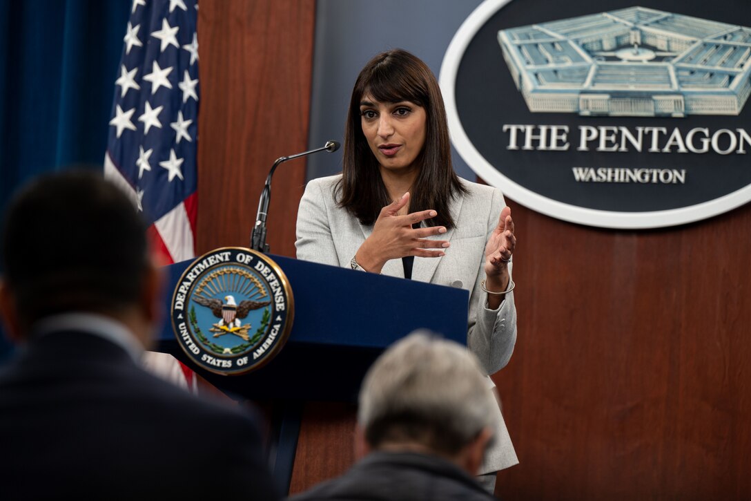 A woman stands behind a lectern to address a crowd of reporters.
