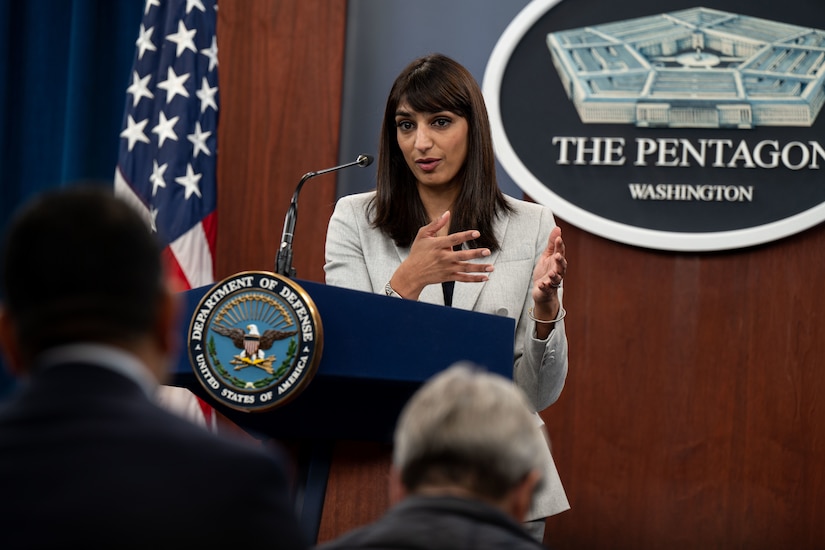 A woman stands behind a lectern to address a crowd of reporters.