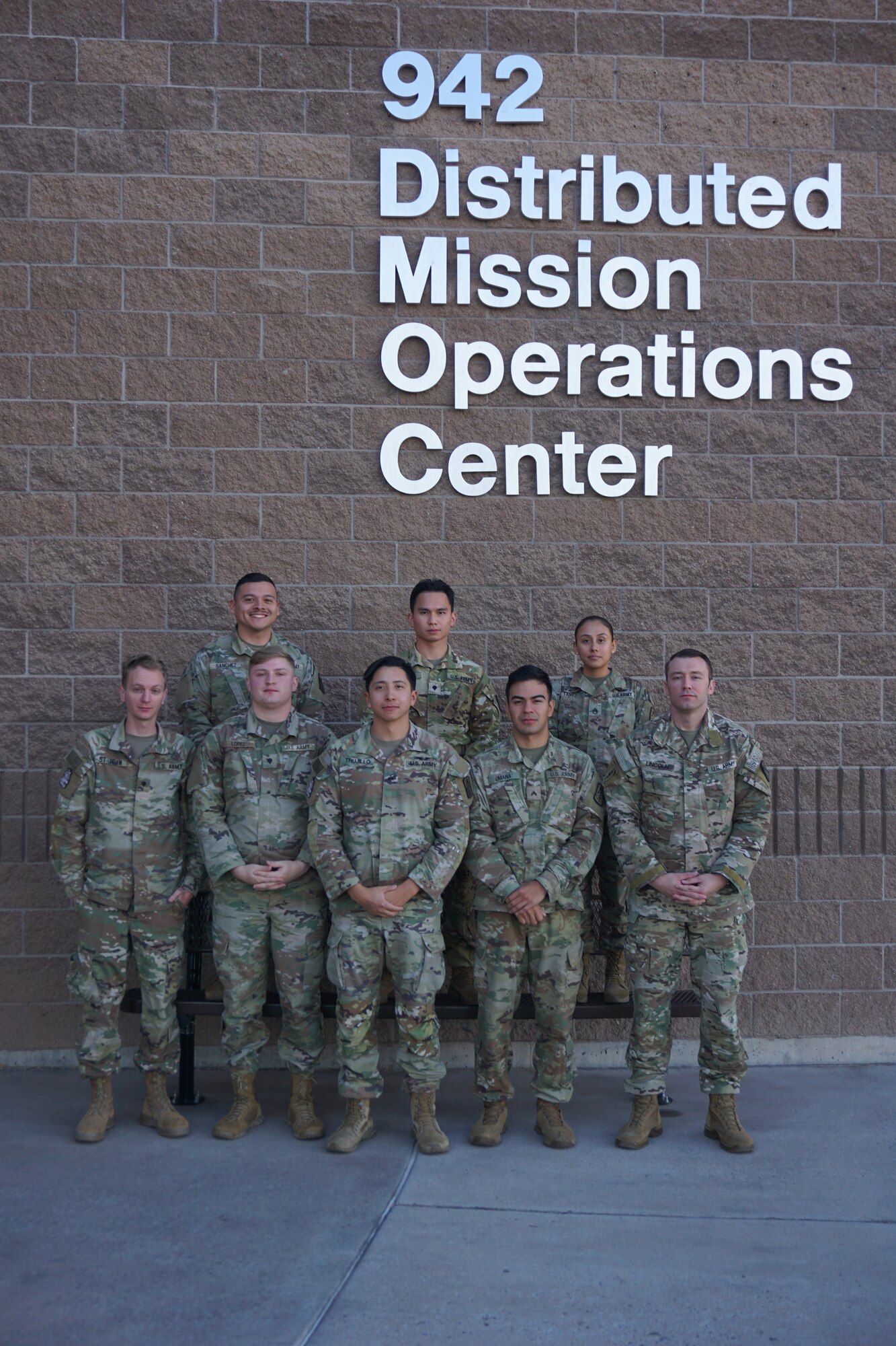 photo: military members stand in a group in front of building with wording “942 Distributed Mission Operation Center”