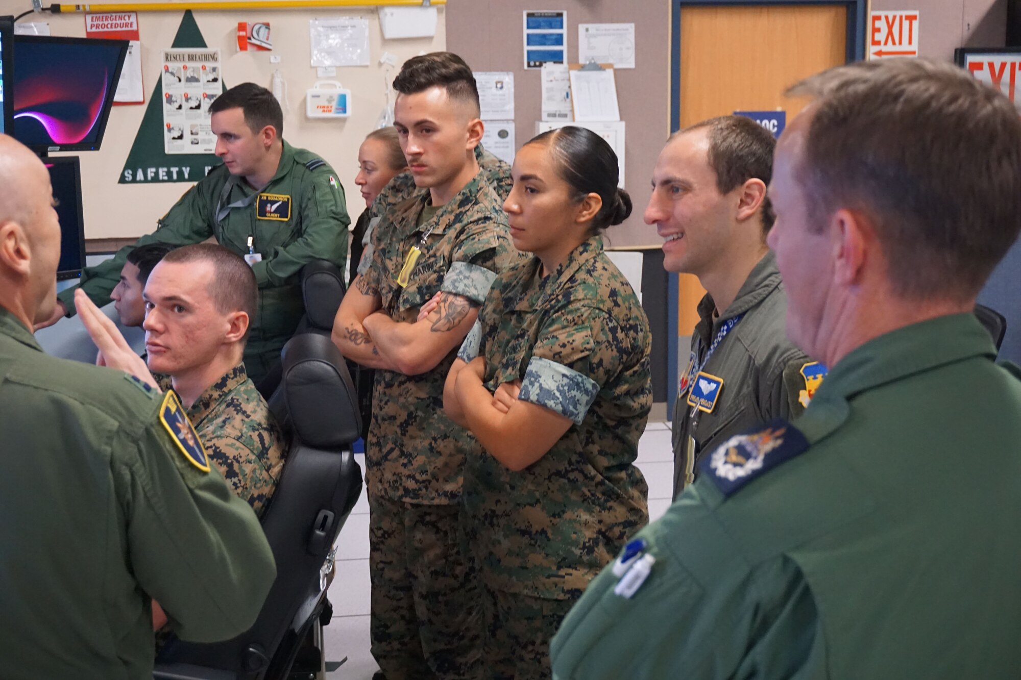 Military members stand behind two military members use flying simulator