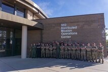photo: military members stand in a group in front of building with wording “942 Distributed Mission Operation Center”