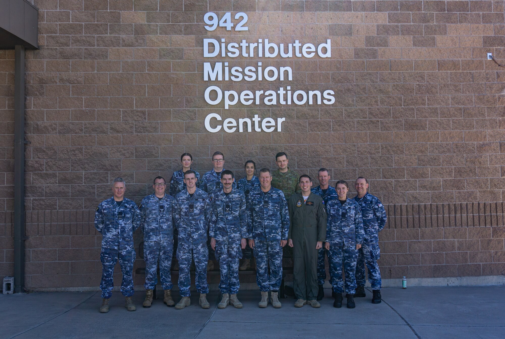 photo: military members stand in a group in front of building with wording “942 Distributed Mission Operation Center”