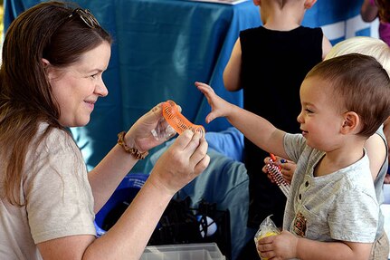 An adult woman holds an orange spring. A small child reaches for the toy.