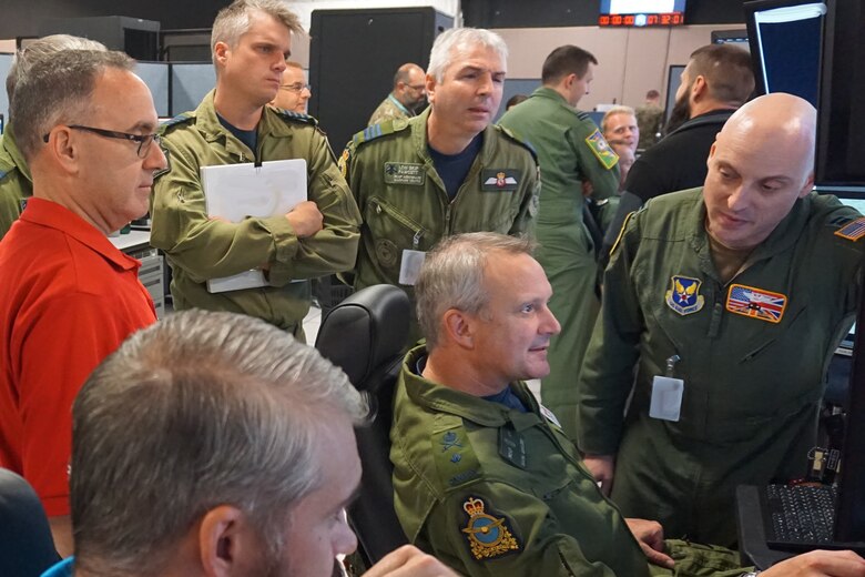 Military members encircle two seated military members looking at simulator screen