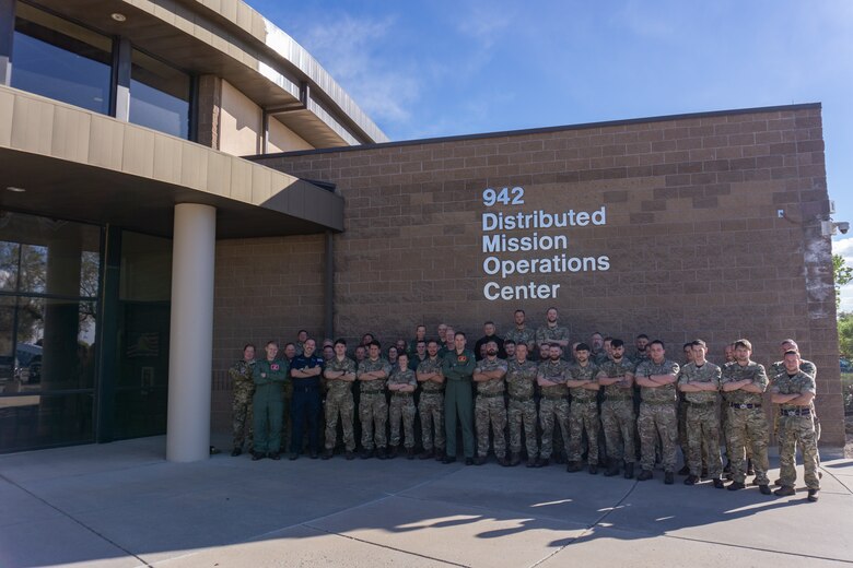 photo: military members stand in a group in front of building with wording “942 Distributed Mission Operation Center”