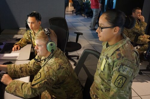 military members sit working at computers while one military member stands behind watching