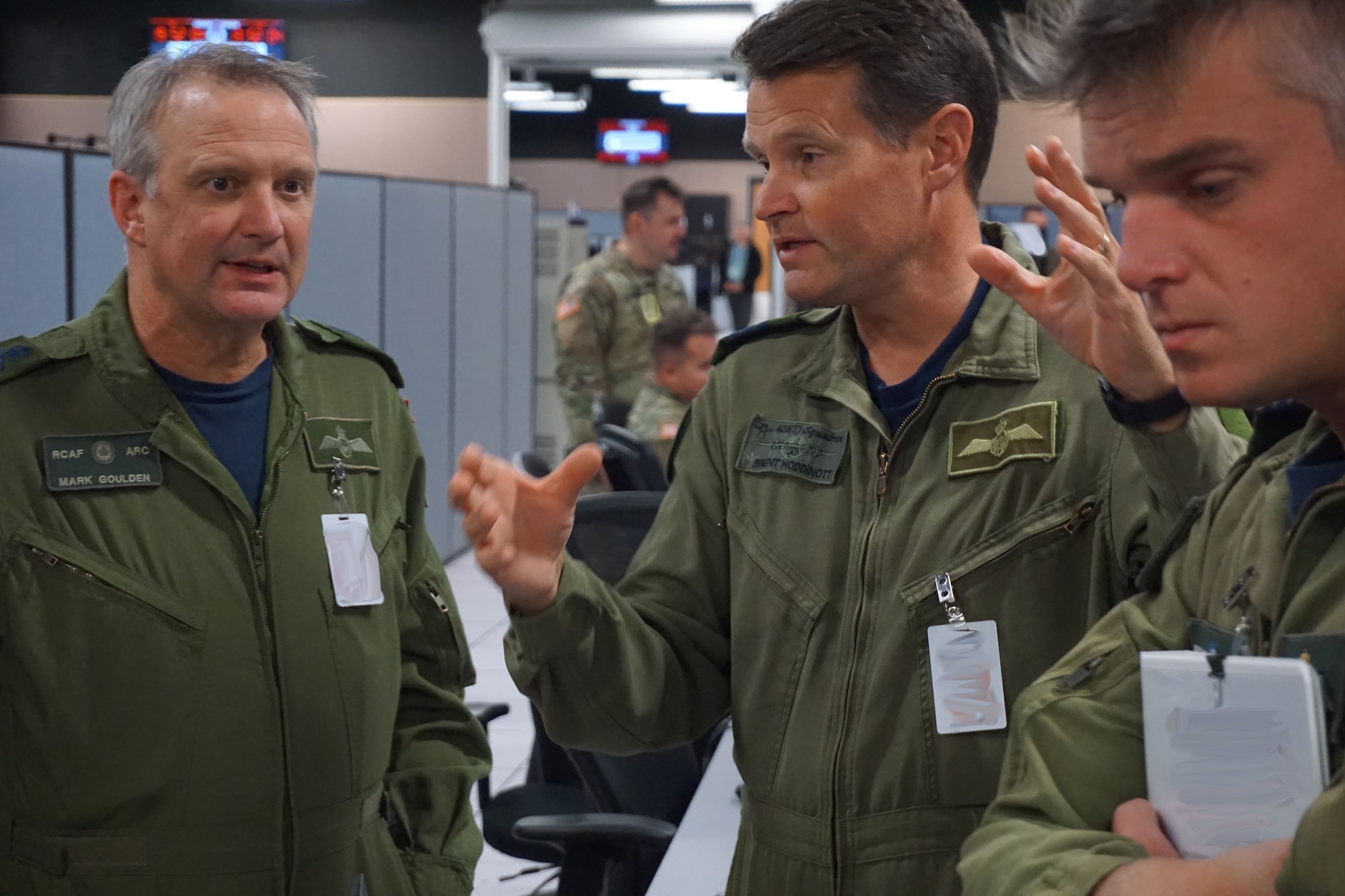 military members stand talking to each other  in an office environment