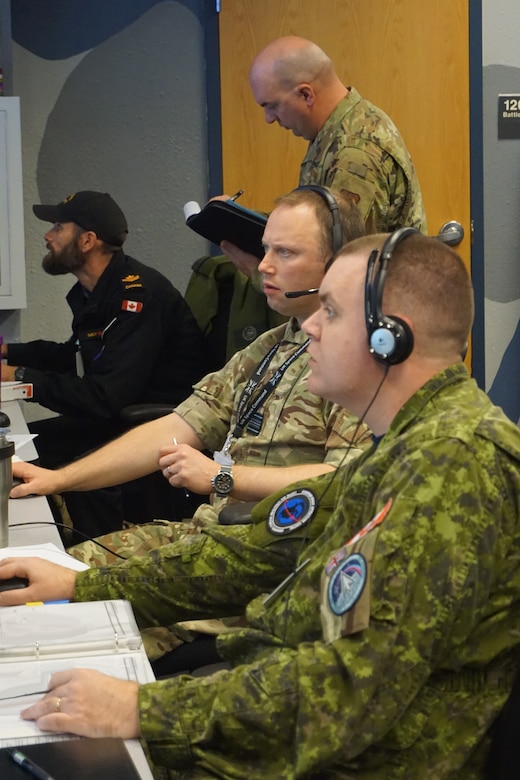 military members sit working at computers while one military member stands behind watching