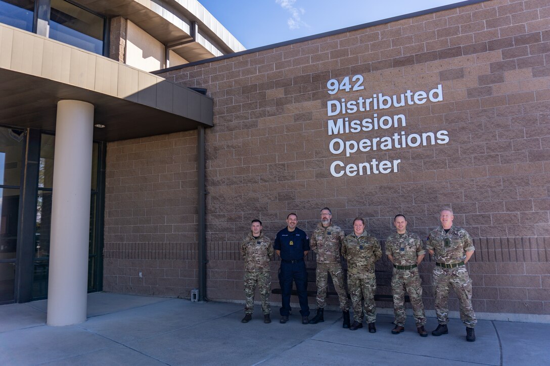 photo: military members stand in a group in front of building with wording “942 Distributed Mission Operation Center”