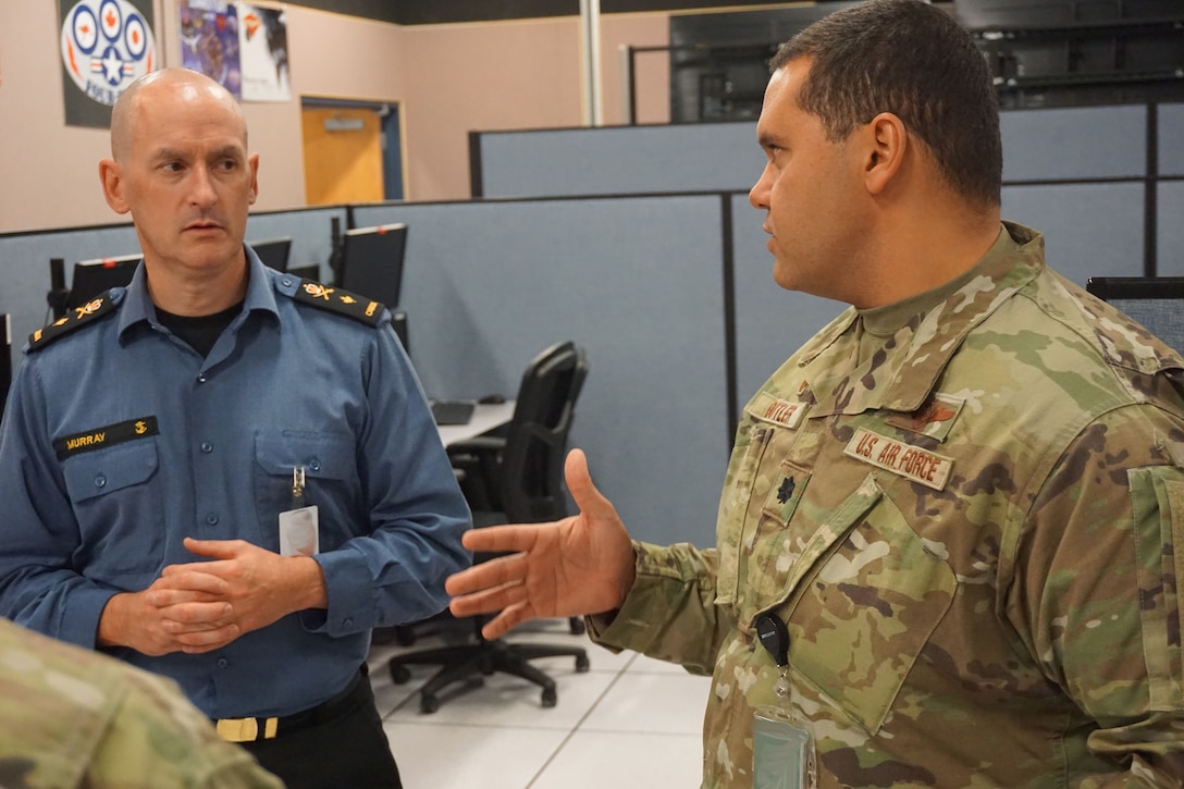 two military members stand talking to each other in an office area