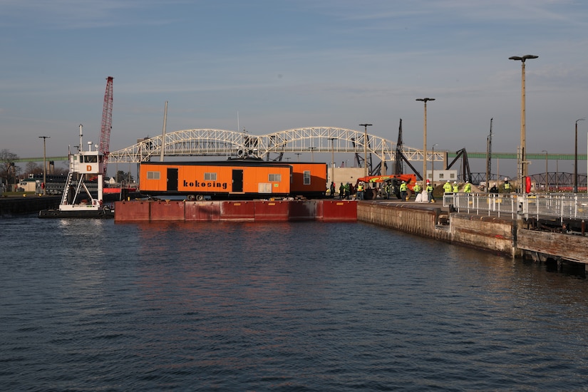 A barge carries four construction trailers through the Poe Lock and delivers them over the lock wall for construction site use.