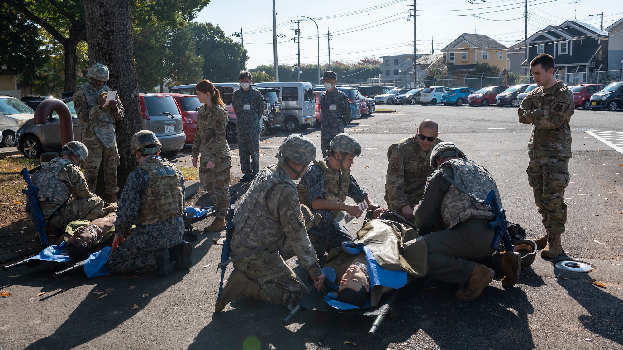 A large group of medics gather around medical training dummies in a parking lot