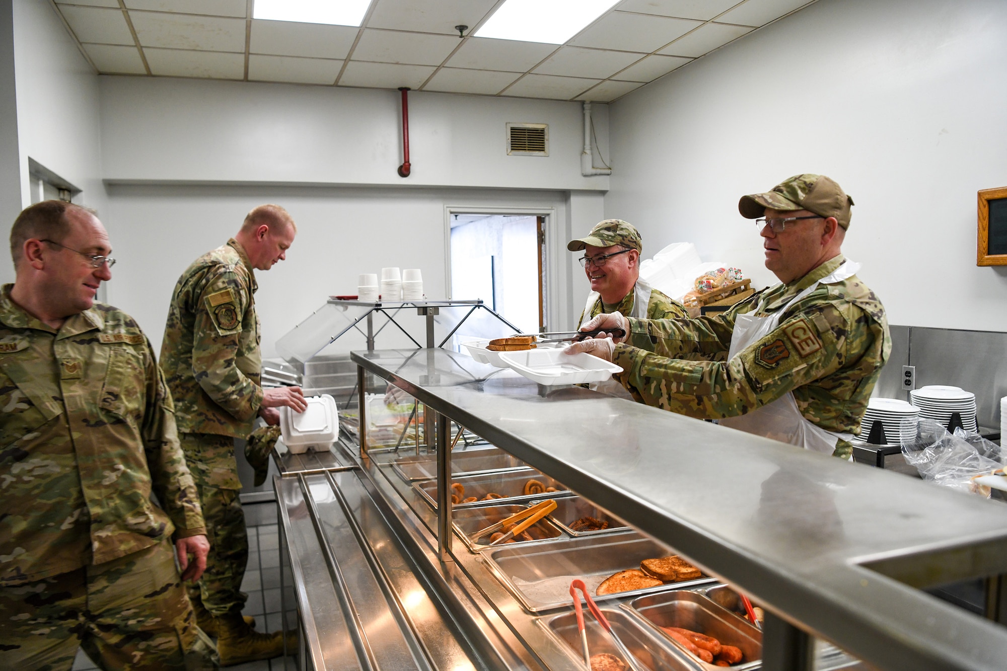 (left to right) 445th Civil Engineer Squadron’s Chief Master Sgts. Chad Lifer, fire department chief and Alan Baker, senior enlisted leader, serve lunch to Airman at the Pitsenbarger Dining Facility, Wright-Patterson Air Force Base, Ohio, Nov 6, 2022. Commanders, first sergeants and chiefs serve Airmen at the dining facility during November unit training assemblies to show their appreciation for their service.