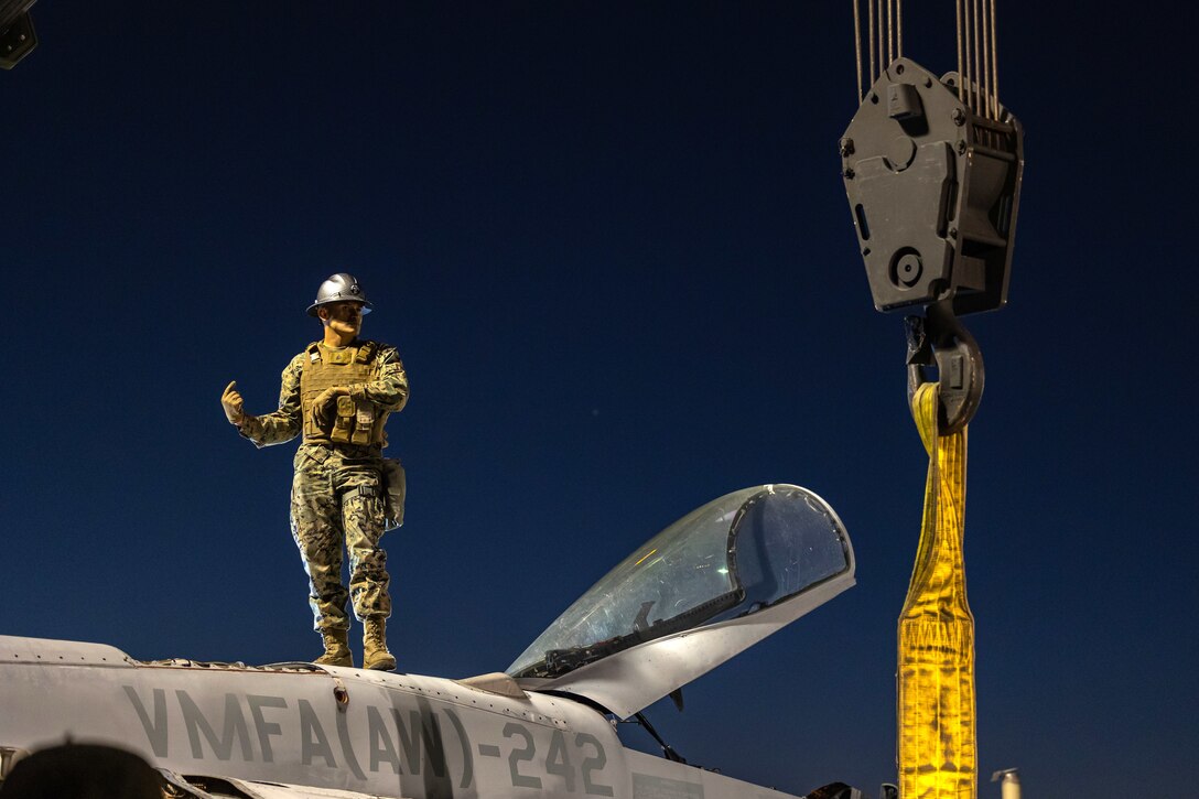 A Marine stands on top of a plane with a crane boom next to it.