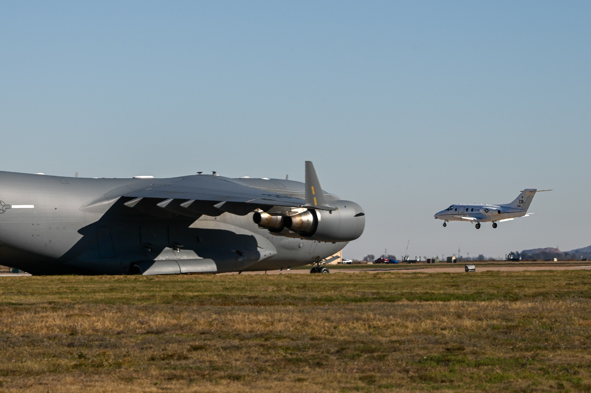 A T-1 Jayhawk lands at Altus Air Force Base, Oklahoma, while a C-17 Globemaster III waits to taxi, Nov. 15, 2022. The T-1 is a medium-range, twin-engine jet trainer used in the advanced phase of specialized undergraduate pilot training for students selected to fly airlift or tanker aircraft. (U.S. Air Force photo by Senior Airman Kayla Christenson)