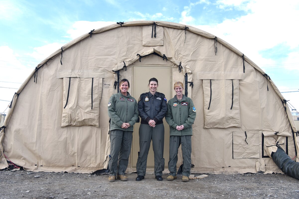Three female commanders stand in front of a tan military tent.