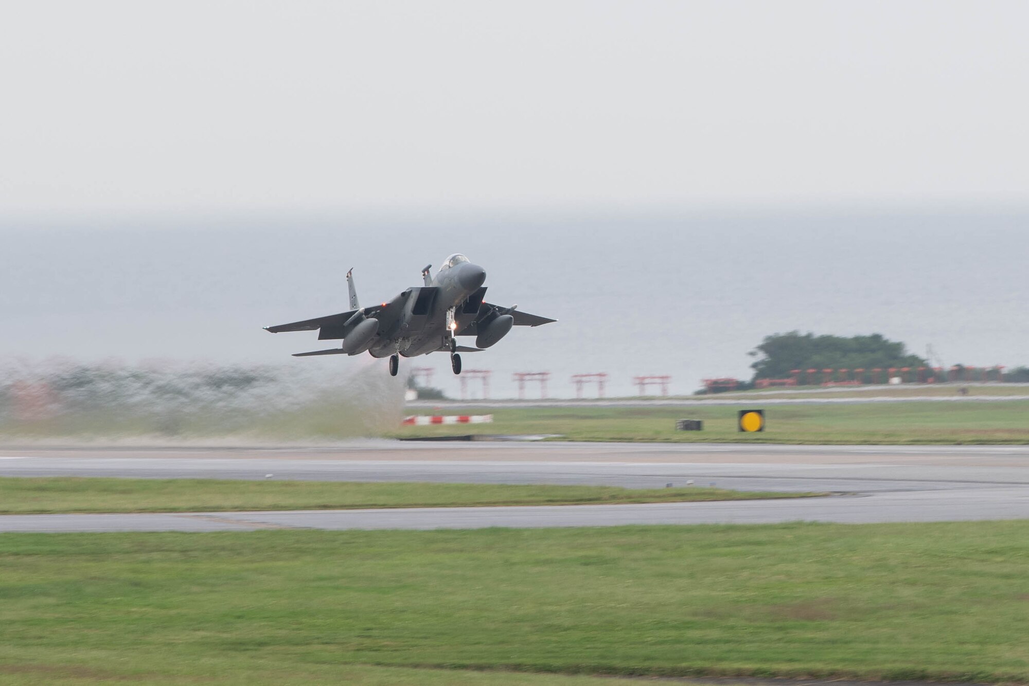A jet flies over runway.