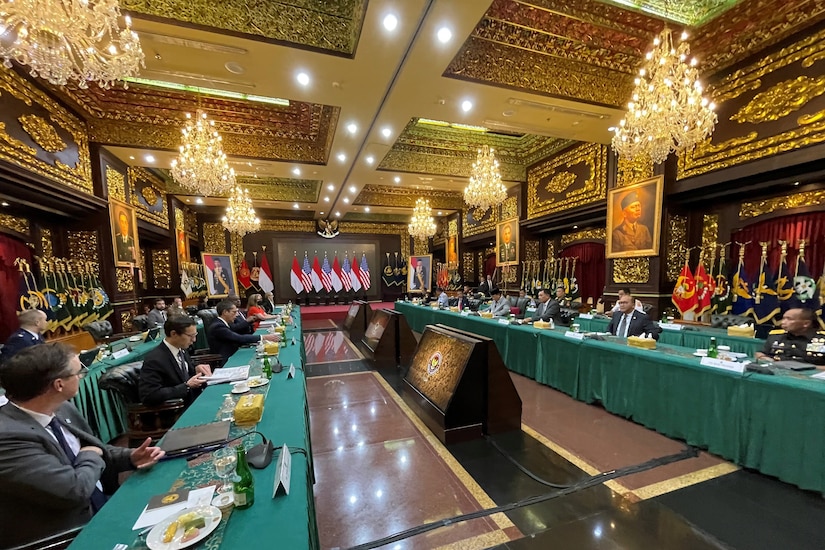 People sit at two long tables in an ornately decorated room.