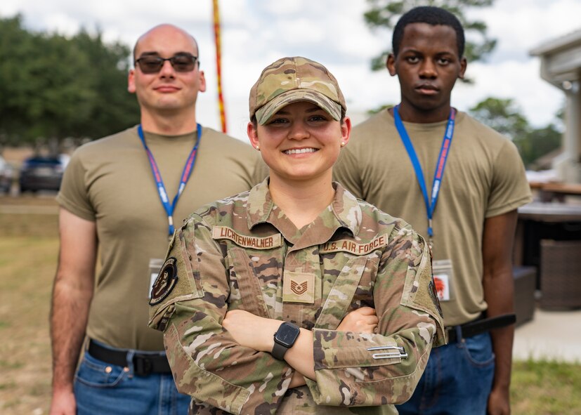 Airman stands in front of two trainees in T-shirts and jeans outdoors.