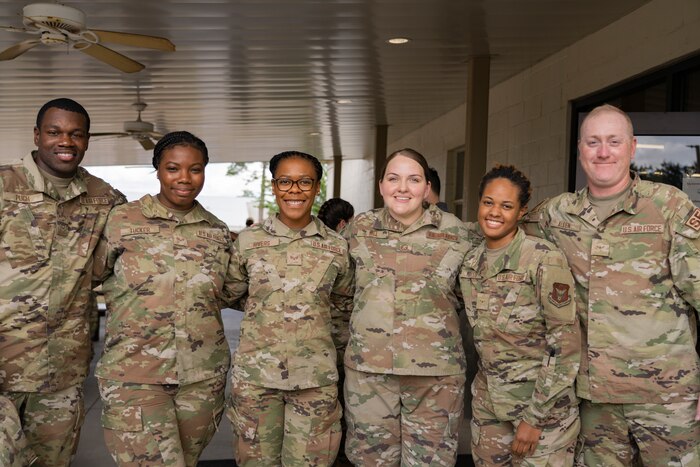 Six Airmen link arms while posing for a photo under an overhang