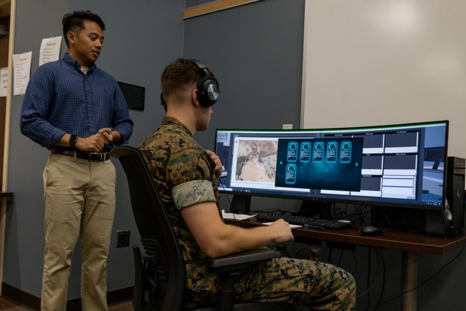 IMAGE: 2nd Lt. Joseph Greer works in the Gaming Environment for Air Readiness (GEAR) prototype, while Software Lead and Naval Surface Warfare Center Dahlgren Division Dam Neck Activity engineer Kyle Tanyag stands by. GEAR uses artificial intelligence and a virtually simulated environment to provide hands-on flexible testing for the U.S. Marines.