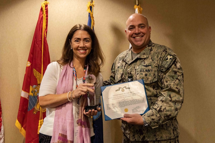 Capt. Daniel Testa, right, Naval Education and Training Assistance Field Activity’s (NETSAFA) commanding officer, presents a Civilian Service Achievement Medal to Ms. Maria Jonckheere, assigned to Training Air Wing Four, at the 29th annual international military student officers (IMSO) conference in Pensacola, Florida, Nov. 15, 2022. Representatives from United States Navy, Marine Corps and Coast Guard met to discuss their critical role in the lives of foreign allies’ students by facilitating their transition to life in a new country and the importance that allied relationships play in maritime security on a global scale. Naval Education and Training Command’s mission is to recruit, train and deliver those who serve our nation, taking them from street-to-fleet by transforming civilians into highly skilled, operational and combat ready warfighters. (U.S. Navy photo by Mass Communication Specialist 2nd Class Zachary Melvin)