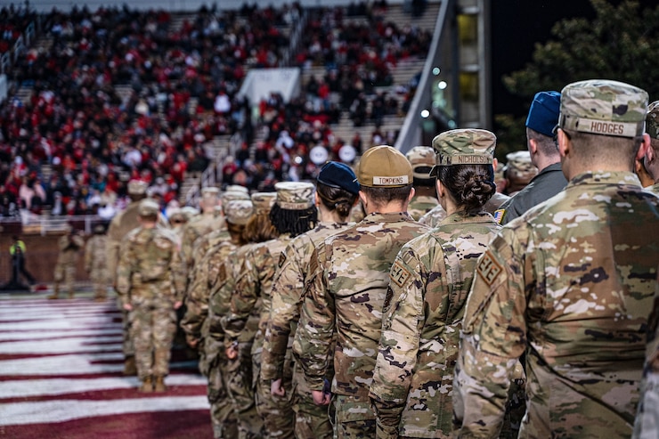 Military members march on football field during half time.