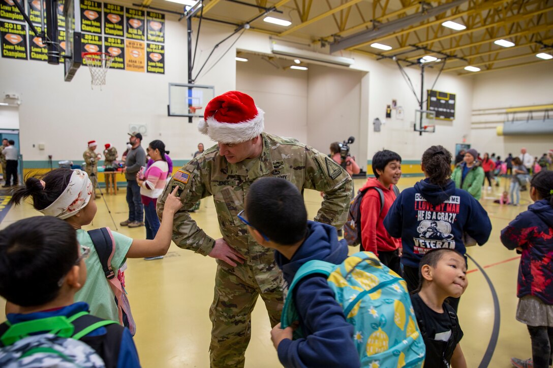 Alaska Army National Guard Staff Sgt. Eddie Jones, left, a Bethel recruiter with the Recruiting and Retention Battalion, answers questions from local children about his uniform patches during Operation Santa Claus in Scammon Bay, Nov. 16, 2022. Operation Santa Claus is the Alaska National Guard’s yearly community relations and support program that provides gifts to children in remote communities across the state. In partnership with the Salvation Army and with more than a dozen volunteers, the program delivered 1,780 pounds of gifts, backpacks, hygiene supplies, and books to 325 children in Scammon Bay. (Alaska National Guard photo by 1st Lt. Balinda O’Neal)