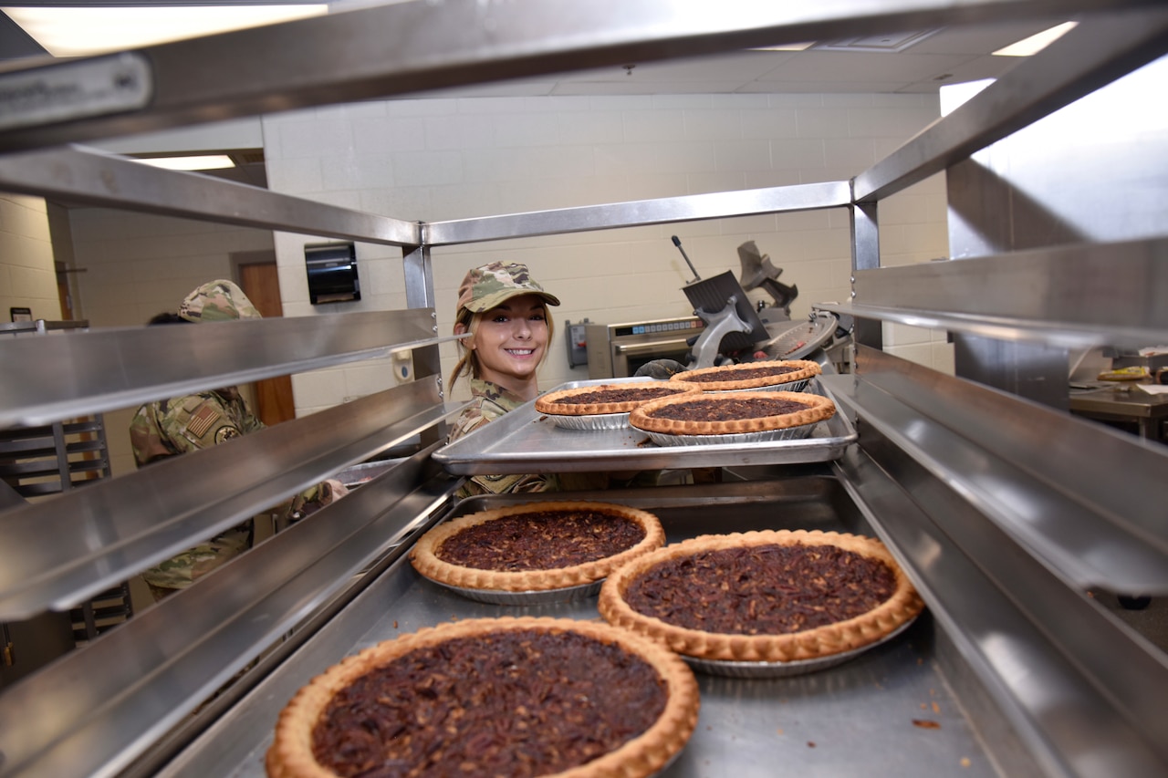 A  service member takes a tray with three pecan pies from a rack containing other pies